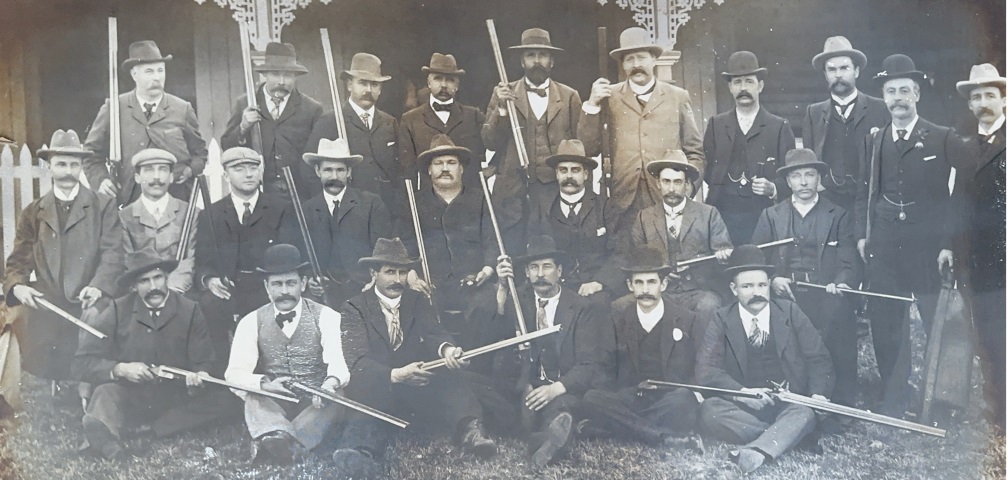 Historic photograph of NSW Gun Club members in suits and hats, posing with their shotguns